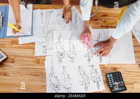 Les mains des tailleurs dessinant des croquis de mode à la grande table en studio, vue du dessus Banque D'Images