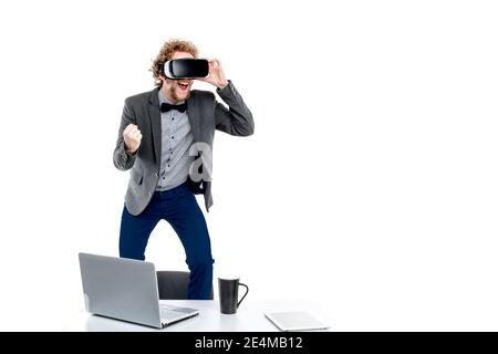 Portrait d'un homme d'affaires élégant aux cheveux bouclés en lunettes vr avec main dans le poing sur la chaise à la table avec des gadgets Banque D'Images