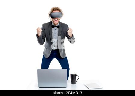Portrait d'un homme d'affaires élégant aux cheveux bouclés en lunettes vr avec main dans le poing sur la chaise à la table avec des gadgets Banque D'Images