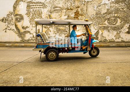 Vue latérale d'un tuk tuk à Bangkok, avec le conducteur portant un masque de protection, contre une goutte arrière d'art mural Banque D'Images