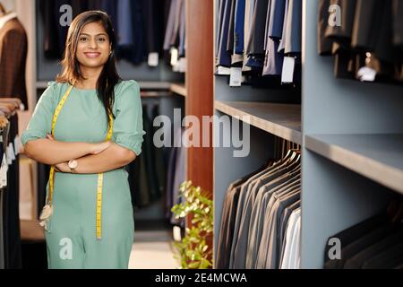 Portrait d'un jeune assistant de magasin indien joyeux debout dans le magasin avec les bras repliés et regardant l'appareil photo Banque D'Images