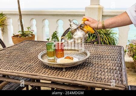 Verser le thé à la menthe dans des verres sur un plateau métallique dans un café de Tanger, au Maroc Banque D'Images