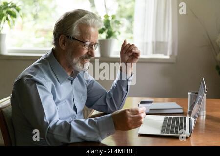 Homme âgé souriant portant des lunettes tenant une carte de crédit, payant en ligne Banque D'Images