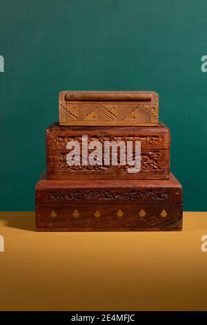 Anciennes boîtes en bois sculptées à la main de couleur marron foncé empilées sur une surface jaune avec un fond vert. Une collection de bois artisanal authentique Banque D'Images