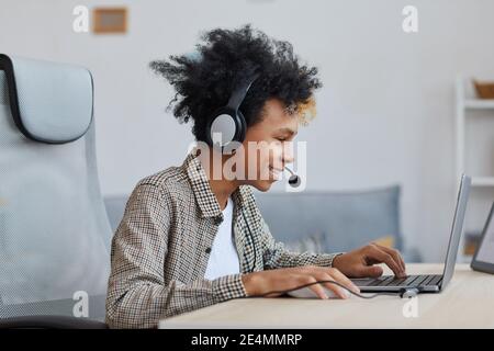 Vue latérale portrait d'adolescent afro-américain jouant des jeux vidéo à la maison et souriant joyeusement, jeune joueur ou blogueur concept, copie espace Banque D'Images