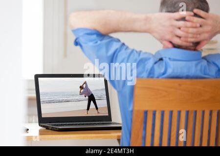 Homme d'affaires à la maison de bureau faisant l'exercice d'étirement ou de détente dans avant de l'ordinateur portable avec homme faisant du yoga sur une plage - mise au point sur l'écran Banque D'Images
