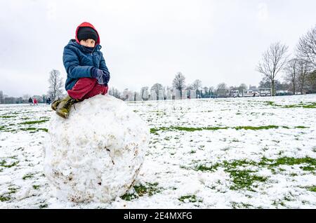 Un garçon est assis sur un énorme rocher de neige dans Prospect Park à Reading, Berkshire, Royaume-Uni. Banque D'Images