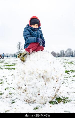 Un garçon est assis sur un énorme rocher de neige dans Prospect Park à Reading, Berkshire, Royaume-Uni. Banque D'Images