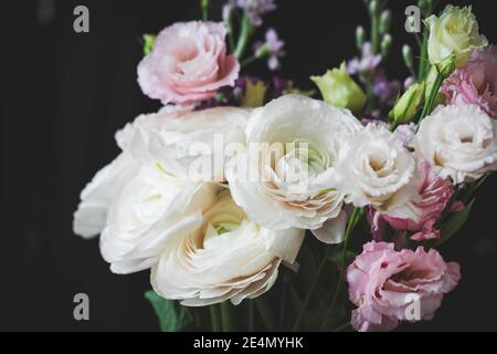 Beau bouquet de fleurs avec ranunculus blanc. Bouquet de mariage sur fond noir, vue rapprochée, tons doux Banque D'Images
