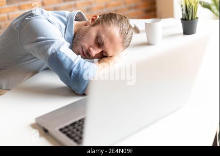 Un employé de bureau de sexe masculin épuisé dans un vêtement chic et décontracté est en train de faire une sieste sur le lieu de travail, se sent fatigué et dévoré, un homme de taille basse dort à la réception Banque D'Images