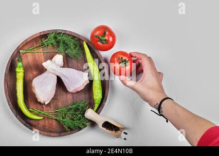 Femme main tenant la tomate juteuse et une assiette de poulet cru jambes avec légumes Banque D'Images