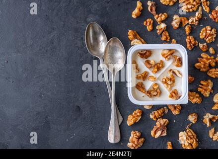 Yogourt blanc dans une tasse carrée en plastique avec noix et cuillères sur fond gris. Vue à plat. Banque D'Images