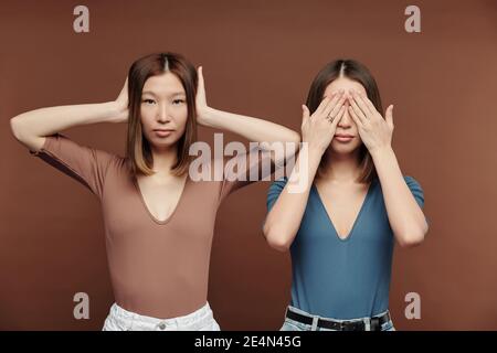 Deux jeunes femmes brunette d'origine asiatique couvrant leurs yeux et des oreilles pour exprimer être sourd et aveugle en se tenant devant l'appareil photo Banque D'Images