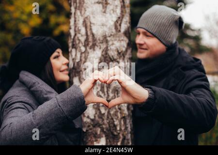 Un jeune couple d'amoureux fait un coeur hors des mains contre un arbre dans la forêt d'automne le jour de la Saint-Valentin. Photo de haute qualité Banque D'Images