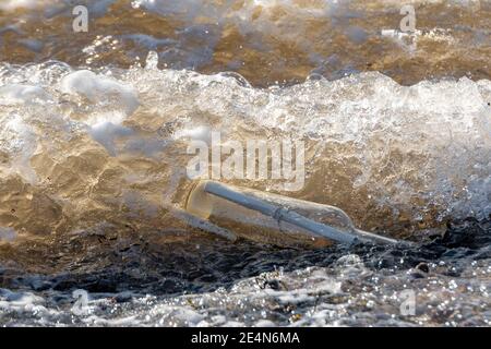 Un message dans une bouteille transparente lavage à terre dans une vague dorée. Jour ensoleillé. Mousse et beaucoup de détails. Bouteille sur le côté. Banque D'Images