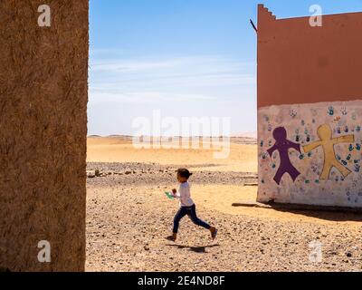 Une jeune fille marocaine court entre deux bâtiments scolaires au Sahara désert en été Banque D'Images