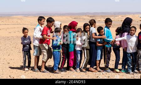 Les enfants s'alignent dans le désert marocain pour entrer dans leur école. Banque D'Images