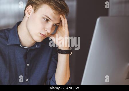 Un jeune homme d'affaires blond ressent du stress sur le lieu de travail au bureau. Les activités de démarrage signifient travailler dur et sans temps pour réussir Banque D'Images