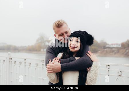 Un couple amoureux marche le long du remblai par temps nuageux, un homme hale une femme contre la toile de fond de la rivière. Photo de haute qualité Banque D'Images