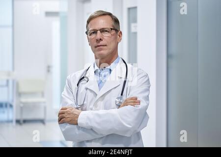 Fiable fier vieux médecin professionnel debout bras croisés à l'hôpital. Banque D'Images