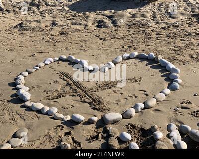 Un coeur fait de rochers sur une plage de sable avec Un X au centre Banque D'Images