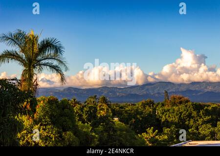 Les montagnes de la Cordillère Septentrionale, baignées de nuages blancs bouffieux, offrent une toile de fond aux palmiers, au feuillage tropical et aux terres agricoles. République dominicaine. Banque D'Images