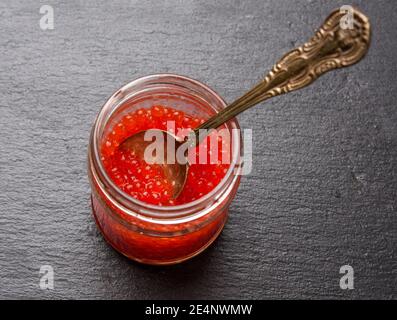 caviar rouge de saumon kéta dans un pot en verre sur une table noire, vue de dessus Banque D'Images