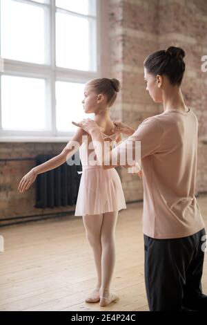 Jeune formateur montrant à son élève la bonne position dans ballet pendant leurs cours en studio de danse Banque D'Images