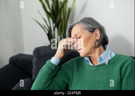 Femme sénior mature à cheveux gris se sentant surtravaillée et fatiguée, souffrant d'une migraine ou souffrant d'un mal de tête sévère, placée la main sur le visage Banque D'Images