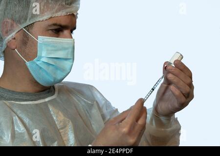 Une infirmière prépare une dose de vaccin à injecter dans un équipement de protection individuelle (EPI). Concept COVID-19 Banque D'Images