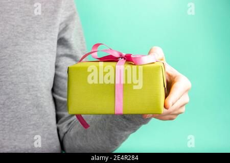 Une main femelle tient un cadeau vert avec un ruban rose. Félicitations pour les vacances. Joyeux anniversaire. Saint Valentin. Cadeau de Noël. Banque D'Images