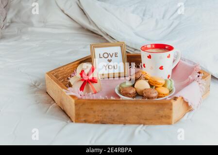Petit déjeuner de la Saint-Valentin au lit pour Lover. Carte Love You dans le cadre, une tasse de café ou de cacao, macarons, boîte cadeau en forme de coeur avec ruban rouge Banque D'Images