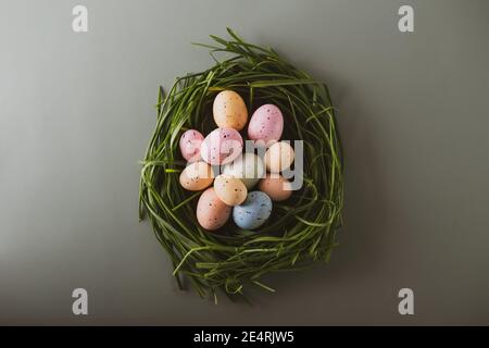 Vue de dessus oeufs de pâques colorés dans l'herbe verte nichent sur le fond vert pâle. Virage vintage. Joyeuses Pâques, concept de printemps. Flat lay, foyer sélectif Banque D'Images