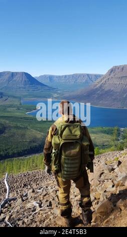 Un touriste se tient avec un sac à dos au-dessus d'une vallée de montagne. Banque D'Images