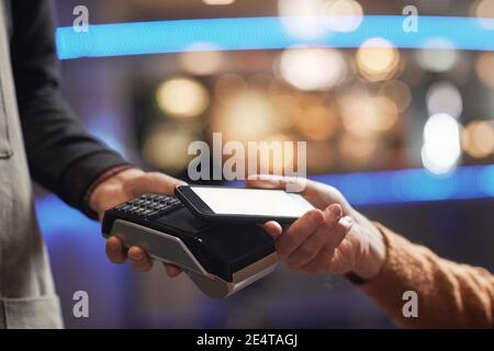 Vue latérale gros plan d'un homme méconnaissable payant avec une carte de crédit, se concentrer sur les mains tenant la carte au-dessus du terminal, espace de copie Banque D'Images