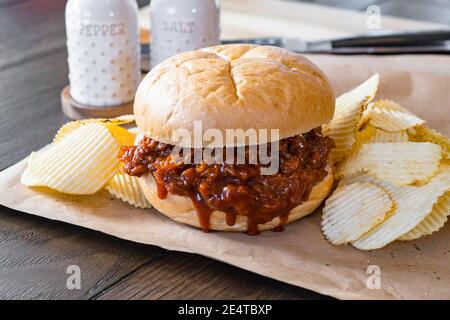 Sandwich barbecue au porc chaud et frais avec chips de pommes de terre sur papier brun Banque D'Images