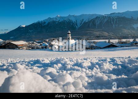 Paysage hivernal ensoleillé idyllique avec une église de village enneigée avec tour d'oignon dans les alpes autrichiennes, Wildermieming, Tirol, Autriche Banque D'Images