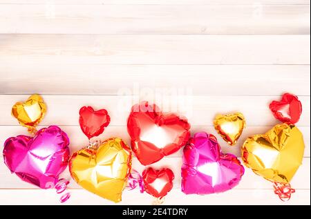 neuf ballons roses, rouges et dorés en forme de coeur avec rubans sur fond blanc et beige en bois. Saint Valentin. Le concept du 14 février. Bannière avec espace de copie. Place pour le texte. Platlay Banque D'Images