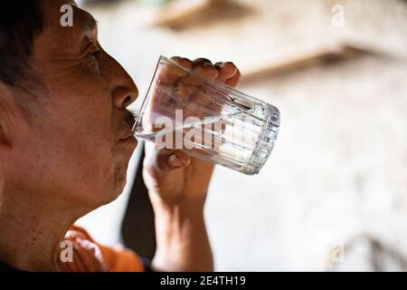 Un homme âgé boit un verre d'eau propre chez lui à San Juan la Laguna, Guatemala, Amérique centrale. Banque D'Images