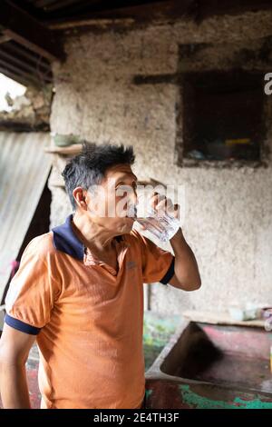 Un homme âgé boit un verre d'eau propre chez lui à San Juan la Laguna, Guatemala, Amérique centrale. Banque D'Images