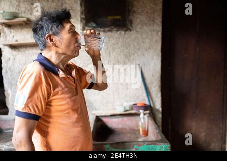 Un homme âgé boit un verre d'eau propre chez lui à San Juan la Laguna, Guatemala, Amérique centrale. Banque D'Images