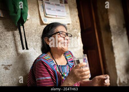 Une femme âgée boit un verre d'eau propre à San Juan la Laguna, Guatemala, Amérique centrale. Banque D'Images