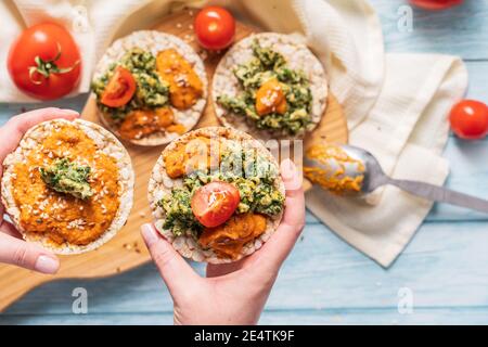 Gâteaux de riz croustillants et soufflés sur la table avec des épinards à tartiner de houmous avec œufs et tomates et légumes sur la table - vue de dessus mains tenant sur un voile sain Banque D'Images