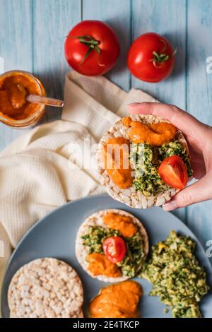 Gâteaux de riz croustillants et soufflés sur la table avec des épinards à tartiner de houmous avec œufs et tomates et légumes sur la table - vue de dessus mains tenant sur un voile sain Banque D'Images
