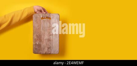 main femelle tenant une planche à découper en bois sur fond jaune Banque D'Images