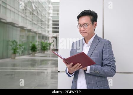 Homme d'affaires asiatique debout et regardant son carnet de rendez-vous. Banque D'Images