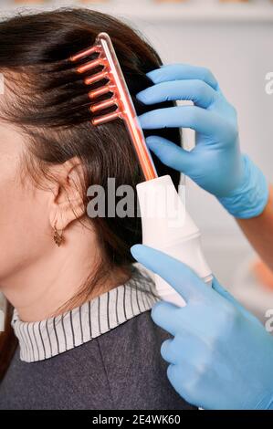 Gros plan du médecin trichologue se brossant les cheveux des clientes avec un appareil de croissance de cheveux au laser. Femme recevant un traitement de cheveux au laser dans un centre médical. Concept de beauté et de soins capillaires. Banque D'Images