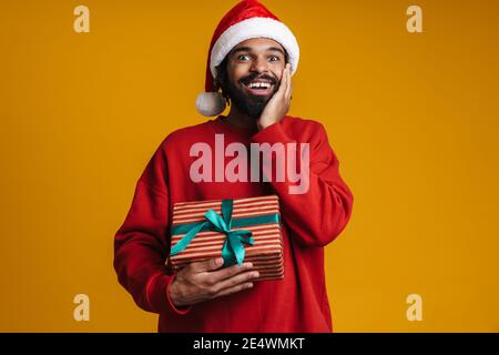 Ravi afro-américain gars dans le chapeau du Père Noël posant avec Cadeau de Noël isolé sur fond jaune Banque D'Images