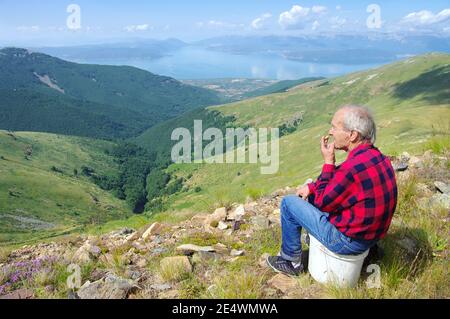 Bitola, République de Macédoine - 24 juillet 2011 : un homme âgé sur la ridgeline du parc national de Pelister fume en s'asseyant devant une terre idyllique Banque D'Images