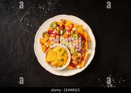 Nachos mexicains avec Chili con carne, guacamole et sauce au fromage, grenaille sur fond noir Banque D'Images